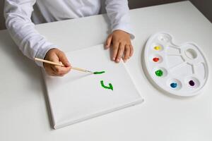Child painting green brush stroke on canvas with color palette photo