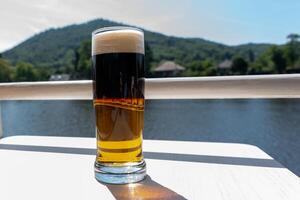 Refreshing beverage in a tall glass beside a serene river with lush green hills in the background photo