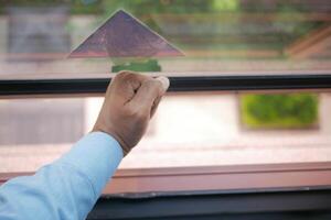 Hand adjusting window pane with outdoor view in daylight photo
