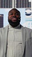 Vertical Black young businessman delivering inspiring business pitch on stage, using hands free microphone to make an important speech. Visionary CEO motivational speaker addresses attendees. Camera B. video