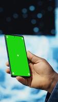 Vertical Focused black IT professional looks at phone with green screen, standing in a digital artificial intelligence environment. Solving deep learning tasks for big data automation. Cybernetics. Camera B. video