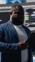 vertical africano americano desenvolvedor trabalhando em programação e automação, codificação em uma computador portátil com uma futurista interface atrás ele. tecnologia profissional prospera dentro uma mundo do ai e código trechos. Câmera b. video