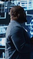 Vertical Modern african american specialist works in AI data visualization environment, illustrating computer science and automation tools for machine learning, neural networks systems. Camera B. video