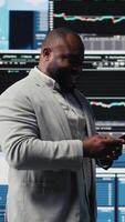 Vertical Young business leader checking online fintech reports on mobile phone, examining infographics for financial insight and development. Young adult browses smartphone apps. Camera A. video