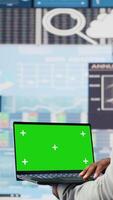 Vertical Black administrator holding device with green screen for analysis, reviewing monthly reports and infographics for company development. Performance metrics for growth, forecasting. Camera A. video