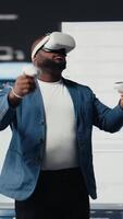 Vertical African american software developer uses virtual reality headset for coding, high tech interface workspace. Surrounded by terminal windows, representing digital programming culture. Camera A. video