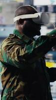 Vertical Black military personnel uses VR glasses to collect intelligence from satellite imagery, working in command control with high tech monitoring tools for a national defense mission. Camera B. video