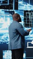 Vertical Black male IT engineer examining digital AI brain interface on dashboard, symbolizing neural networks, science and algorithmic thinking. Cybernetics for high tech machine learning. Camera A. video