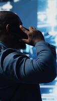 Vertical African american IT expert answers phone call to discuss deep learning through neural networks and automation systems. Chatting on telephone line for predictive analytics science. Camera B. video