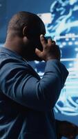 Vertical Black tech specialist talking on smartphone call in an AI powered environment, representing predictive algorithms and machine learning systems. Working on automation and innovation. Camera B. video