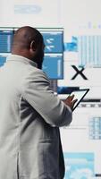 Vertical African american businessman in a digital environment focused on graphs, working on strategic planning analysis for profitability and performance. Insightfulness and fintech forecasting. Camera A. video