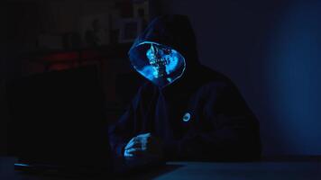 Face covered hacker using laptop in dark interior depicting cybersecurity threat and digital warfare video