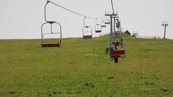 Single Person Riding Chairlift on Grassy Hill With Red and Yellow Seats, Summer Mountain Resort Scene Showing Open Cable Lift Ascending to Upper Station With video