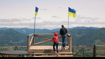 People Standing on Scenic Wooden Platform With Ukrainian Flags, Enjoying Panoramic Mountain View in Carpathians Under Clear Sky on Windy Day With Rolling Green video