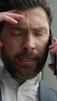 Vertical view unhappy frustrated Caucasian middle-aged business man talking mobile phone call failure upset in office worry stressed 40s businessman male talk smartphone problem suffering headache video