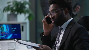 Worried stressed African American businessman employee manager talking mobile phone cellphone call discuss consult client reading business contract document paperwork trouble worker in office report video