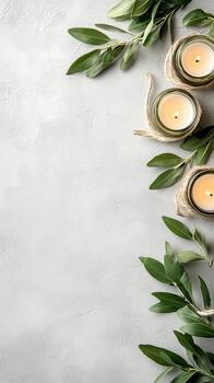 Burning candles in glass jars wrapped with string, adorned with fresh green leaves, arranged on a textured grey surface. Peaceful and tranquil arrangement. photo