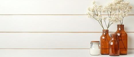 Dried white flowers displayed in brown glass bottles near a full glass jar on a white wooden surface against a wall photo