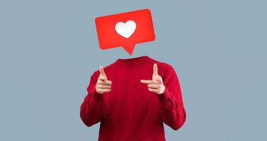 A person in a red sweater gestures playfully while displaying a heart icon instead of their head, symbolizing social media engagement and connection. The backdrop is minimal and modern. photo