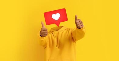 Individual enthusiastically shows thumbs up with large heart icon instead of head. The vibrant yellow background adds energy, perfect for expressing positivity and likeability on social media. photo