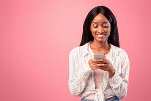 Online life concept. Attractive black woman using smartphone on pink studio background. Pretty African American lady browsing web, sending message, chatting with friend, checking social media photo