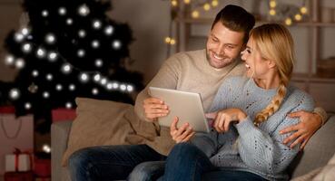 Loving couple having fun together at home on xmas, sitting on couch and using digital tablet, copy space photo