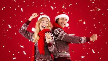 Joyful millennial couple dancing on Christmas or New Year party over red background with falling confetti. Panorama photo