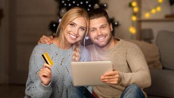 Joyful man and woman making purchases online, using digital tablet and credit card, xmas atmosphere at home photo