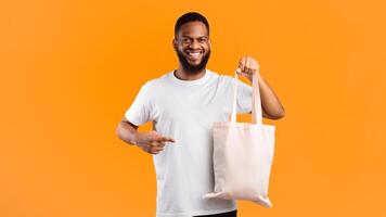 No More Plastic. Smiling Black Guy Holding Textile Eco Bag Standing Over Yellow Background In Studio. Ecology And Consumerism, Eco-Friendly Plastic-Free Lifestyle Concept. Panorama photo