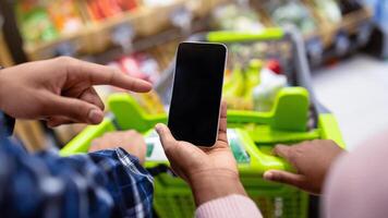 Unrecognizable black couple holding smartphone with empty screen at supermarket, mockup for your mobile app or website. African American guy and lady with cellphone shopping at mall photo