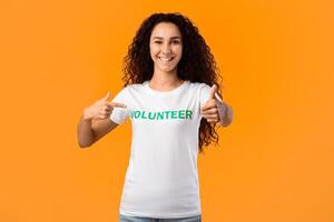 Happy Female Volunteer Gesturing Thumbs-Up Pointing At Herself Posing Standing On Yellow Studio Background, Smiling To Camera. Female Activist Showing Like Approving Volunteering Work photo