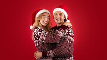 Expressing affection. Lovely young couple in Santa hats and Christmas sweaters hugging on red background photo