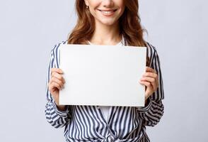 Unrecognizable young lady holding blank sheet of paper in hands, smiling woman demonstrating empty placard with copy space for your text or design, posing over light background, closeup view photo