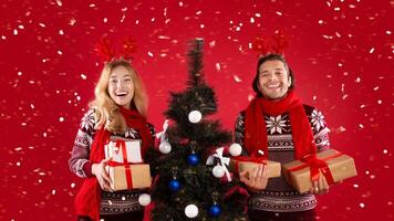 Portrait of happy young couple with Christmas tree and gifts on red background photo