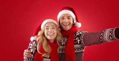 Happy young guy with his girlfriend in Christmas outfits taking selfie over red background photo