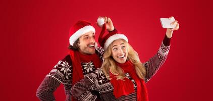 Xmas holiday. Beautiful girl and her boyfriend having fun while taking selfie on cellphone over red background photo