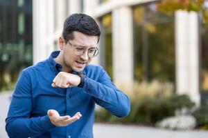 A man wearing glasses uses a smartwatch to talk using an app on the street in front of a building photo