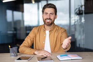 A smiling businessman extends his hand in a welcoming gesture at his desk in an office setting, ready to shake hands. photo