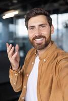 A man smiles during a call, wearing a casual shirt and expressing himself with gestures photo