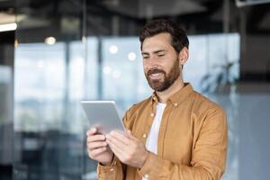 A smiling businessman holds a tablet in a modern office setting, demonstrating engagement and technology use. photo