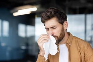A man with a beard blowing his nose with a tissue, possibly suffering from allergies or a cold. photo