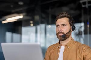 Customer service representative wearing headset working in modern office. Man focused on screen, providing support and assistance. Professional environment setting perfect for remote communication. photo