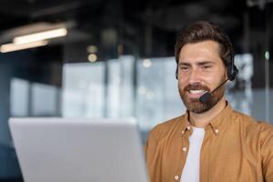 Smiling businessman in office wearing headset working on computer. Professional engaged in remote work, showcasing positive attitude and focus in modern workplace. Ideal for business concepts. photo