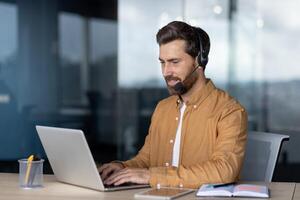 Mature businessman wearing headset engaged in conference at office. Confident professional using laptop for online communication, showcasing skills in remote work and digital collaboration. photo
