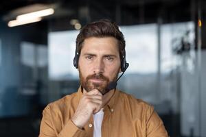 Mature businessman wearing headset focused on communication in modern office setting. Professional attitude, engagement in customer service, and expertise in business communication conveyed. photo