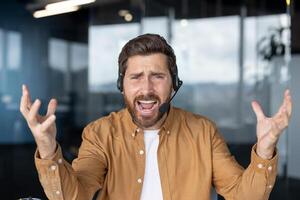 Businessman wearing headset looking frustrated handling a difficult customer support call. Professional man displaying feelings in tech office setting. Concept service communication. photo
