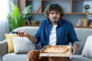 A disappointed man sits holding a pizza and phone, likely ready to complain about delivery. He's clearly unhappy photo