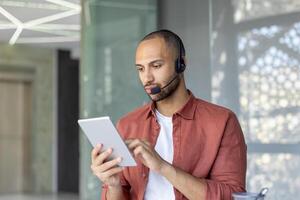 A man wearing a headset uses a tablet indoors, possibly in a customer service or support setting. photo