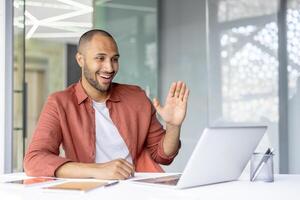 Successful businessman at workplace using laptop for call. Man at workplace inside office, greeting colleagues and partners remotely. Business meeting online conference. photo
