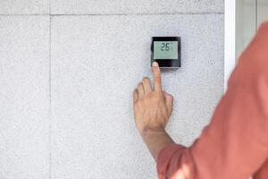 A person adjusts the temperature on a smart thermostat mounted on a textured wall photo